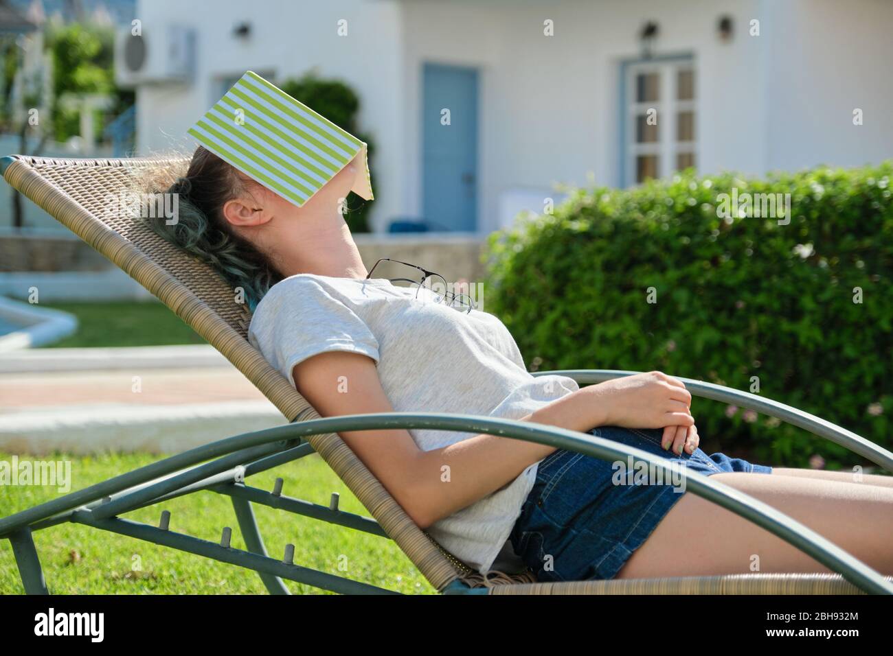 Un adolescente cansado dormido en la tumbona con un libro. Durmiente niña  en el día soleado, en césped verde en el jardín. Descanso, entrenamiento,  sueño saludable durante el día, jóvenes Fotografía de