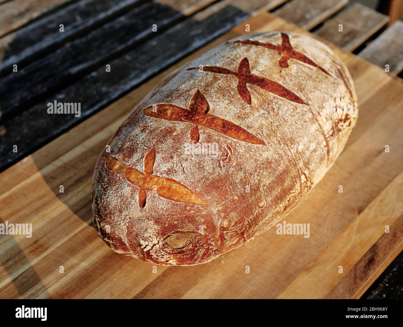 Pan de masa fermentada recién horneado en la tabla de cortar de bloque de carnicero exterior Foto de stock