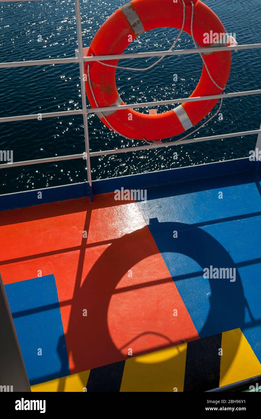 la boya naranja cuelga en la barandilla de un ferry, sombras en tierra colorida, fuerte contraste de color, rojo y azul Foto de stock