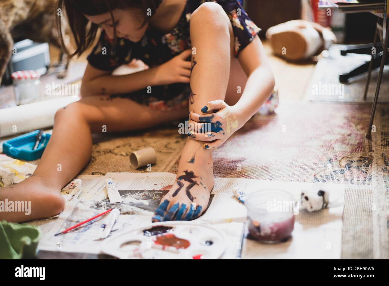 Niña jugando en casa y pintando su pie y mano. Foto de stock