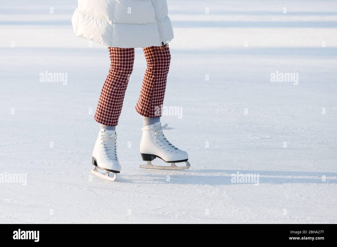 Primer plano de piernas de mujer con pantalones de cuadros rojos en patines en una pista de patinaje abierta, espacio para copias. Día soleado. Deportes de invierno en la ciudad Foto de stock