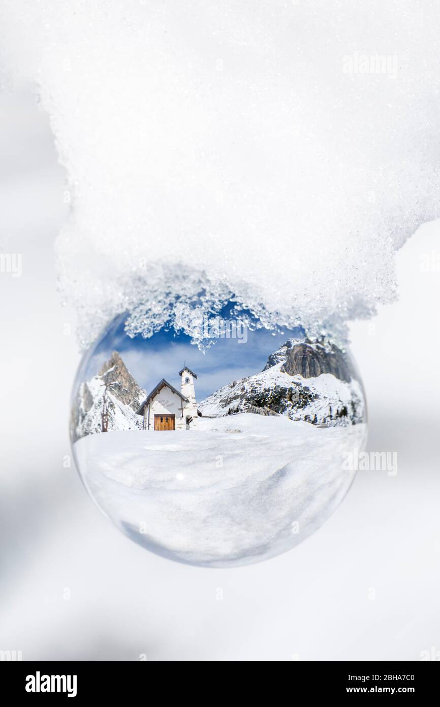 la iglesia alpina en el paso del falzarego en invierno, reflejado a través de una esfera cristalina, cortina d'ampezzo, belluno, veneto, italia Foto de stock