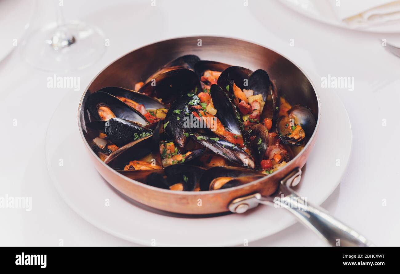 Mejillones hervidos en un plato de cocina de cobre sobre fondo blanco de primer plano Foto de stock