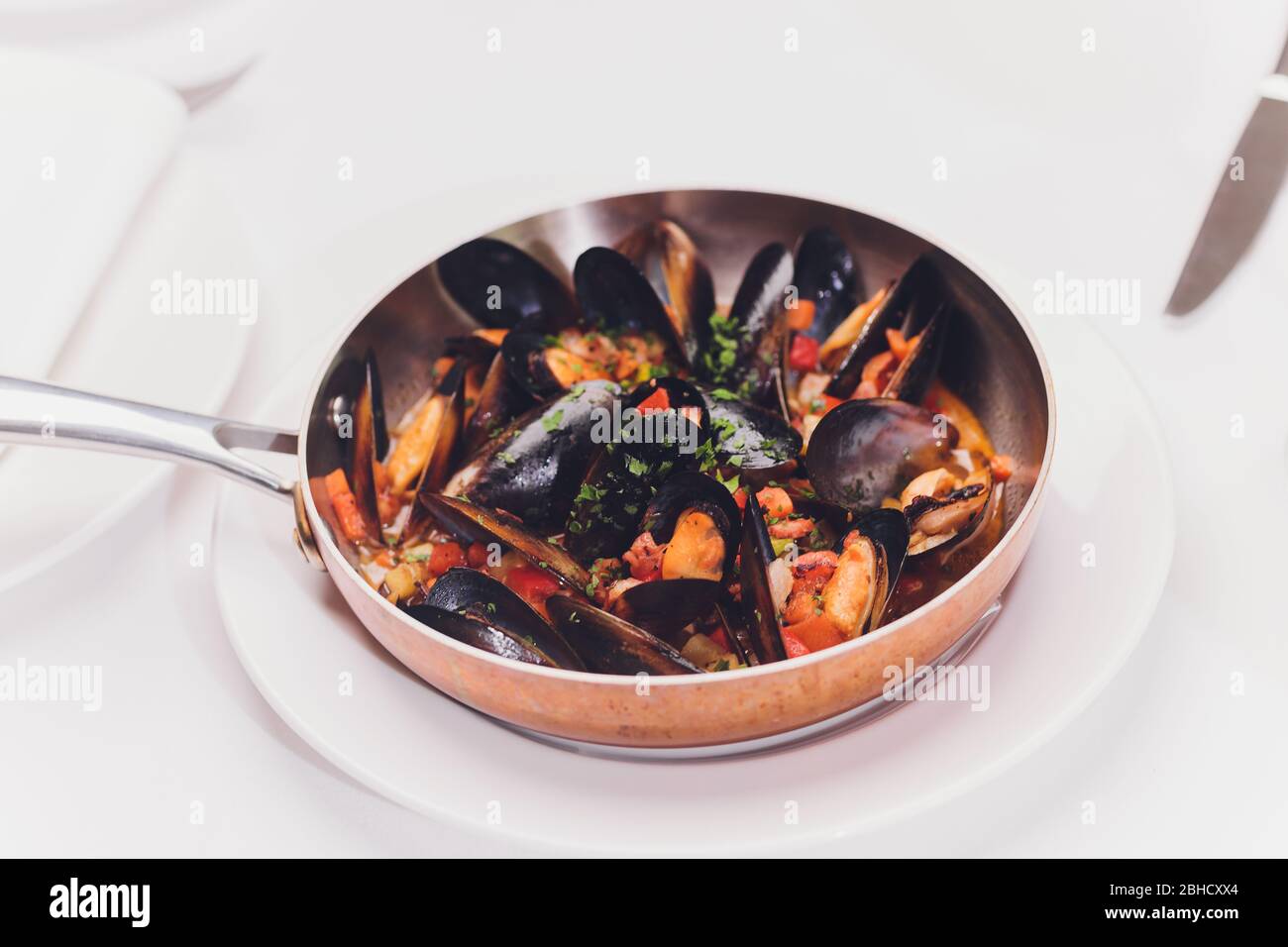 Mejillones hervidos en un plato de cocina de cobre sobre fondo blanco de primer plano Foto de stock