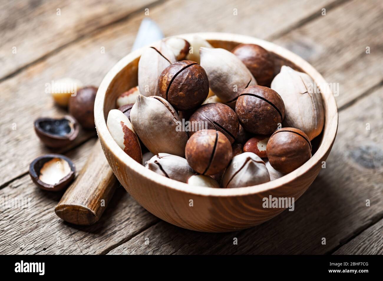 Nueces mixtas secas en un cuenco de madera de primer plano. Nueces de macadamia, pacán y Brasil con cuchillo sobre mesa de madera. Disparo macro de estudio. Foto de stock