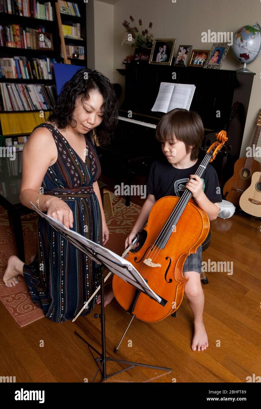 Austin Texas USA, 2012: La madre japonesa instruye a su hijo japonés-americano de 8 años cómo leer partituras mientras practica tocando el violonchelo en casa. ©Marjorie Kamys Cotera/Daemmrich Photography Foto de stock