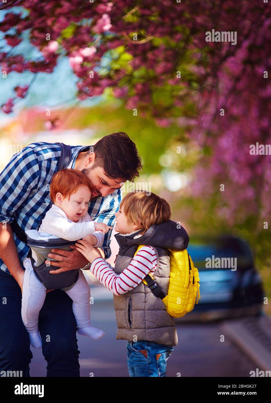 padre feliz con los niños en el paseo en la ciudad de primavera, portabebes, licencia paterna Foto de stock