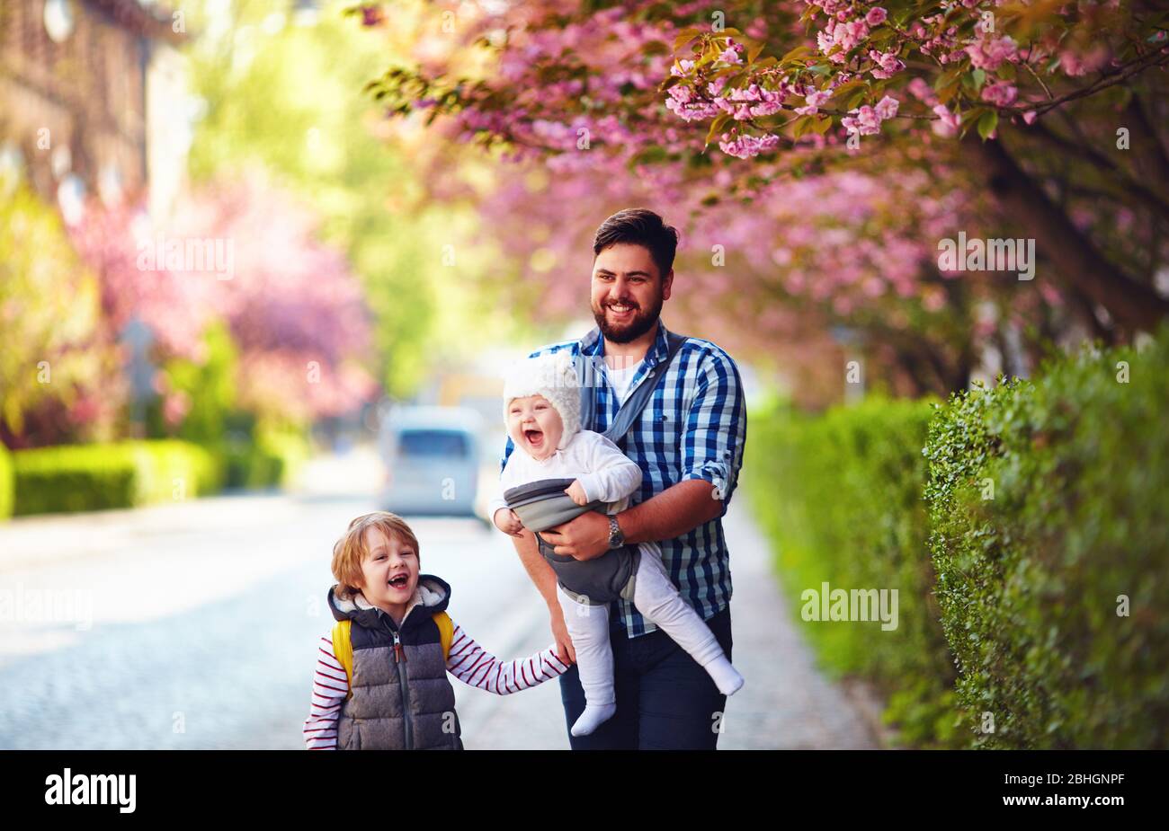 padre feliz con los niños en el paseo en la ciudad de primavera, portabebes, licencia paterna Foto de stock