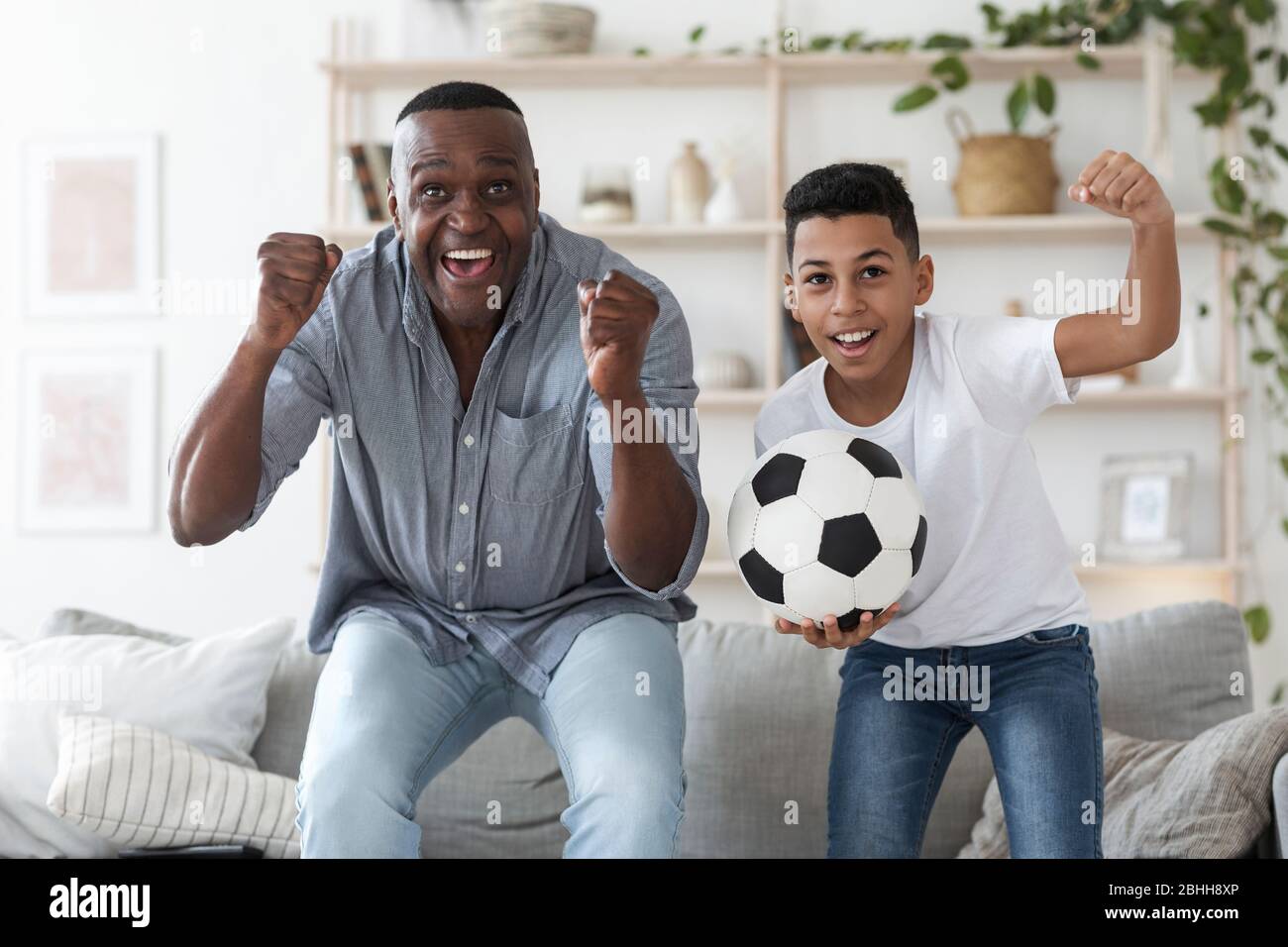 Niño preadolescente negro viendo un partido de fútbol en la televisión con su abuelo Foto de stock