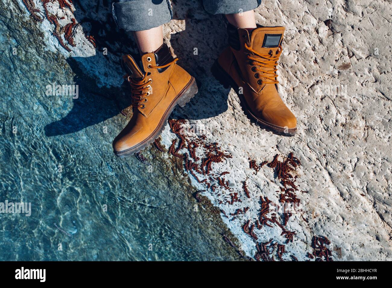 Mujer irreconocible con botas amarillas de trekking se sienta en la costa  cerca de aguas turquesa, vista superior. Aventura, scout, descubrimiento,  concepto de explorador Fotografía de stock - Alamy