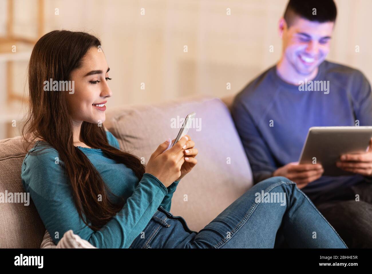 Pareja sentada en el sofá usando la tableta y el teléfono celular Foto de stock