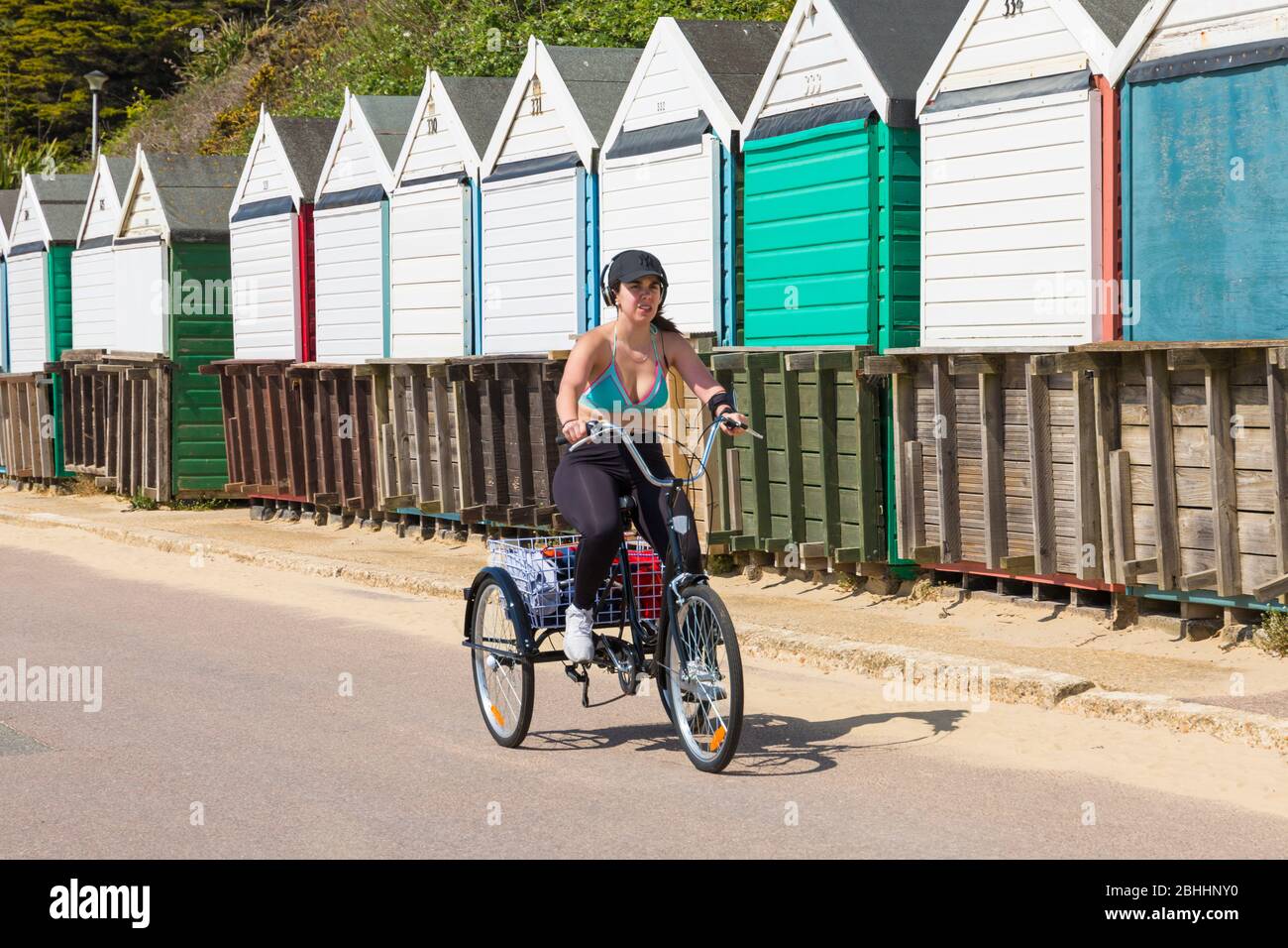 Bournemouth, Dorset Reino Unido. 26 de abril de 2020. El tiempo en el Reino Unido: Un día soleado y cálido como las temperaturas suben en las playas de Bournemouth en la costa sur como la gente toma su ejercicio permitido, la mayoría de los adheridos a las directrices de Coronavirus. Las playas están prácticamente desiertas mientras la policía y los trabajadores del consejo patrullan la zona. Mujer ciclismo a lo largo del paseo marítimo en triciclo pasado cabañas de playa - bicicleta bicicleta trike triciclo ciclista. Crédito: Carolyn Jenkins/Alamy Live News Foto de stock