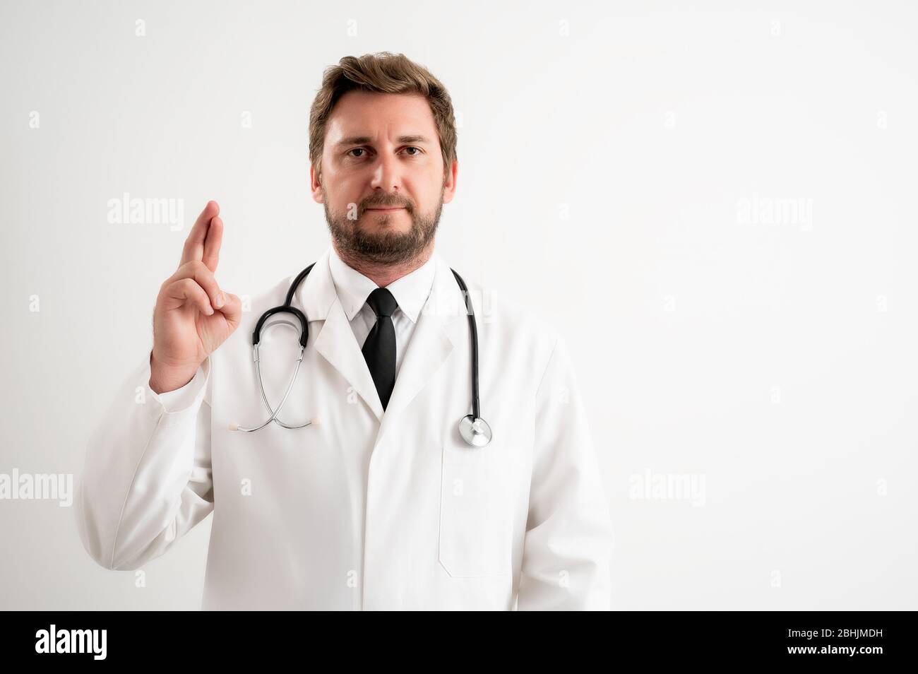 Retrato de un médico masculino con estetoscopio en uniforme médico que muestra buena suerte posando sobre un fondo blanco aislado Foto de stock