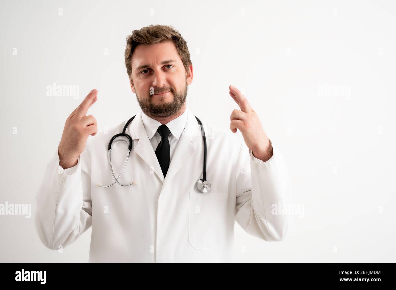 Retrato de un médico masculino con estetoscopio en uniforme médico mostrando doble buena suerte posando sobre un fondo blanco aislado Foto de stock