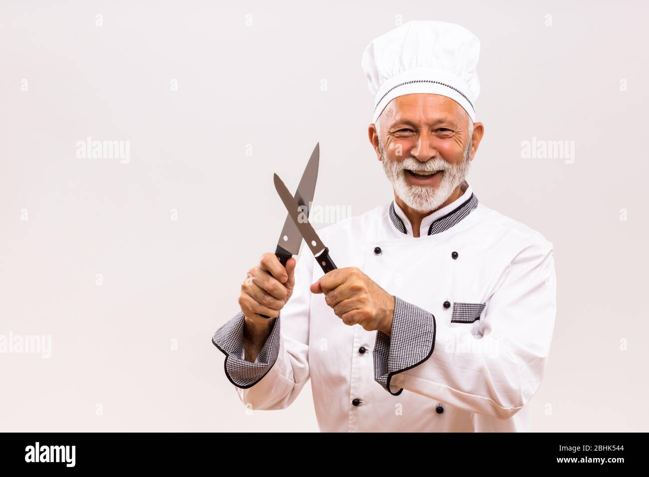 Imagen de chef feliz afila cuchillos sobre fondo gris. Foto de stock