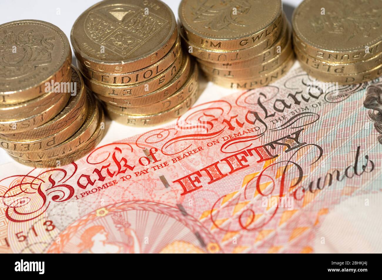Imagen ilustrativa de una nota de £50 libras y pilas de monedas. Foto de stock