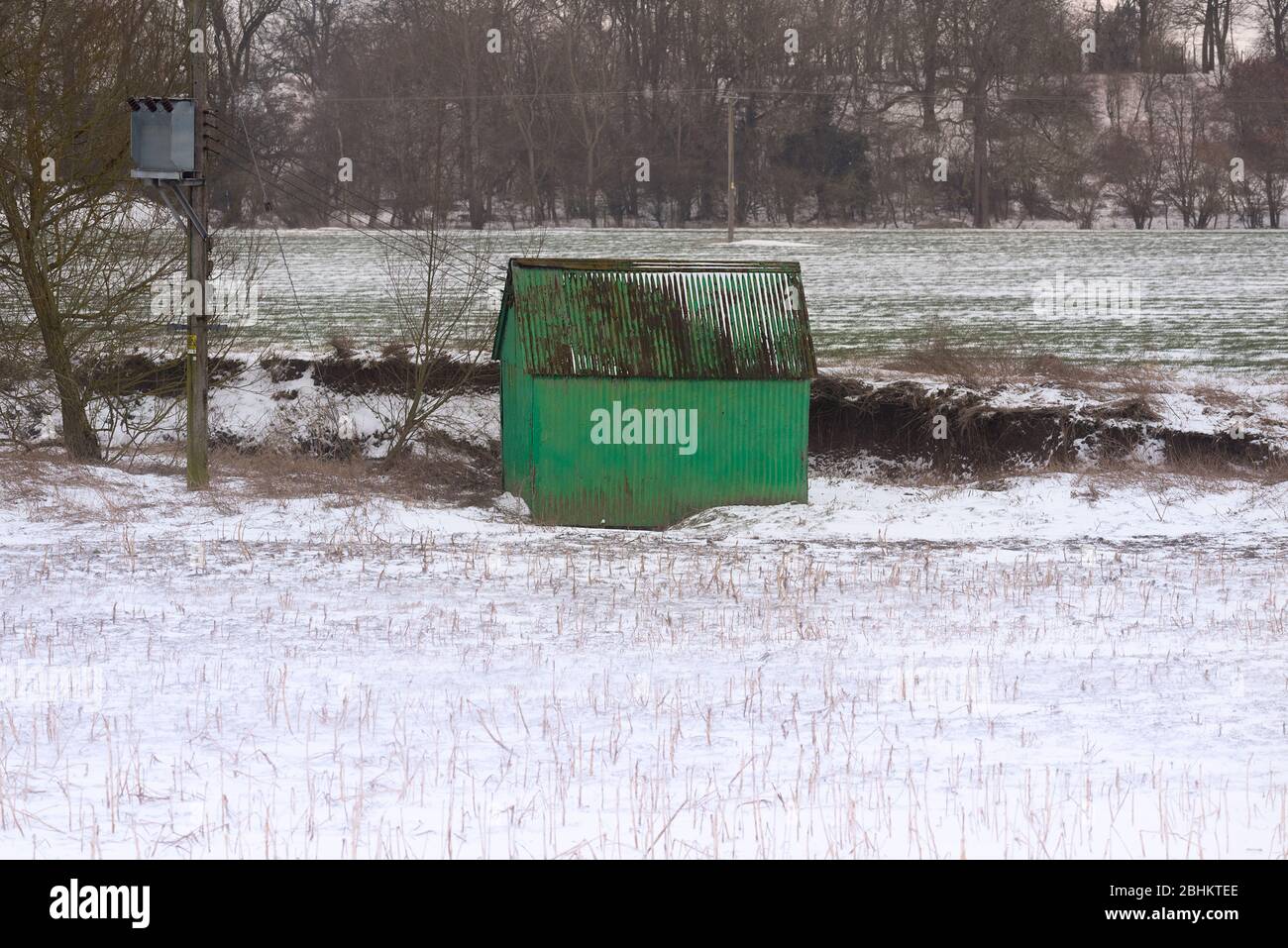 Un viejo cobertizo de metal pintado de verde se encuentra en un campo de agricultores cubierto de una nieve ligera. Foto de stock
