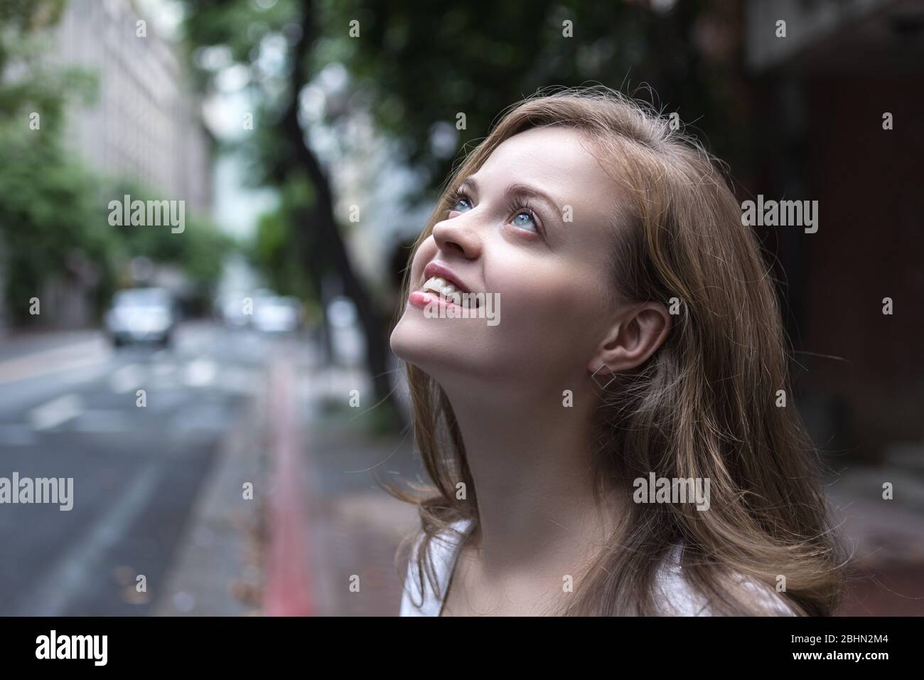 Retrato de una chica hermosa con mirada misteriosa, flirty, coquetiche en su rostro con la calle de la ciudad en el fondo Foto de stock
