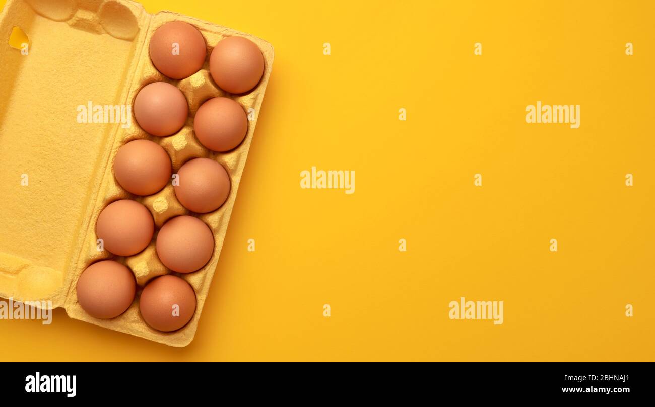 Huevos de pollo marrones en caja de cartón sobre fondo amarillo, vista superior Foto de stock