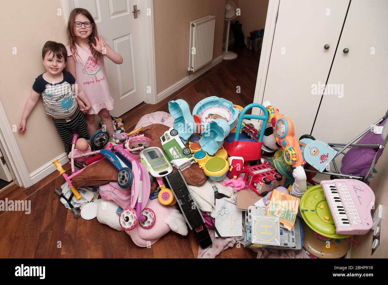 Dos hermanos rodeados por una enorme pila de juguetes infantiles en casa Foto de stock