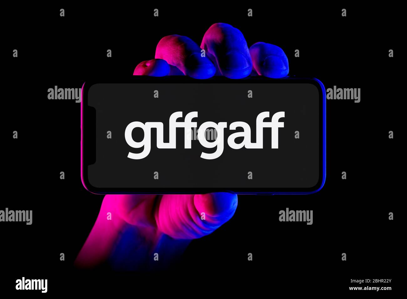 Un smartphone que muestra el logotipo de Giffgaff se sostiene con una toma de mano sobre un fondo negro (sólo para uso editorial). Foto de stock