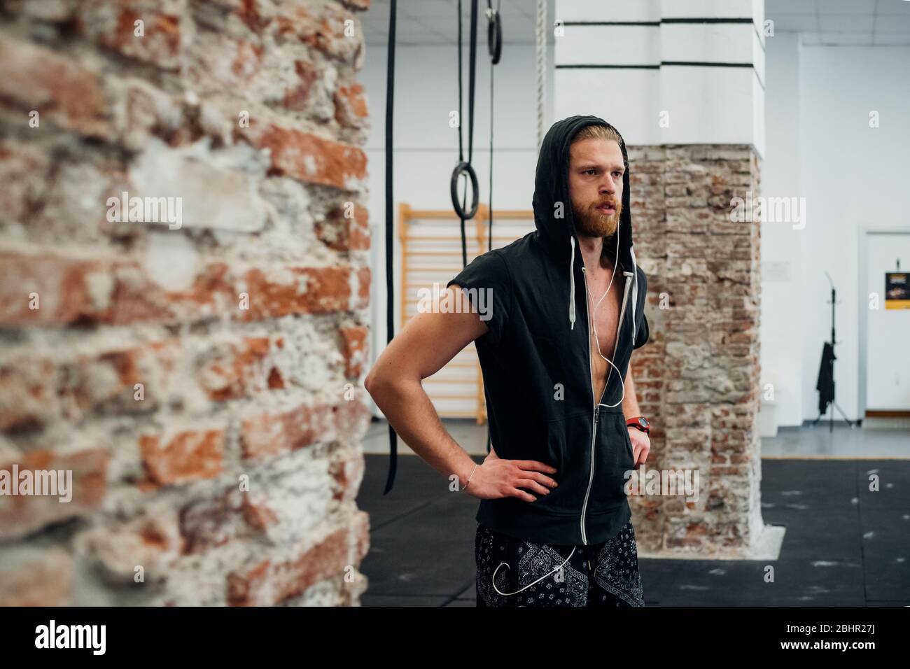 Un hombre con una sudadera con capucha negra con auriculares en sus oídos, en un gimnasio con las manos en sus Fotografía de stock - Alamy