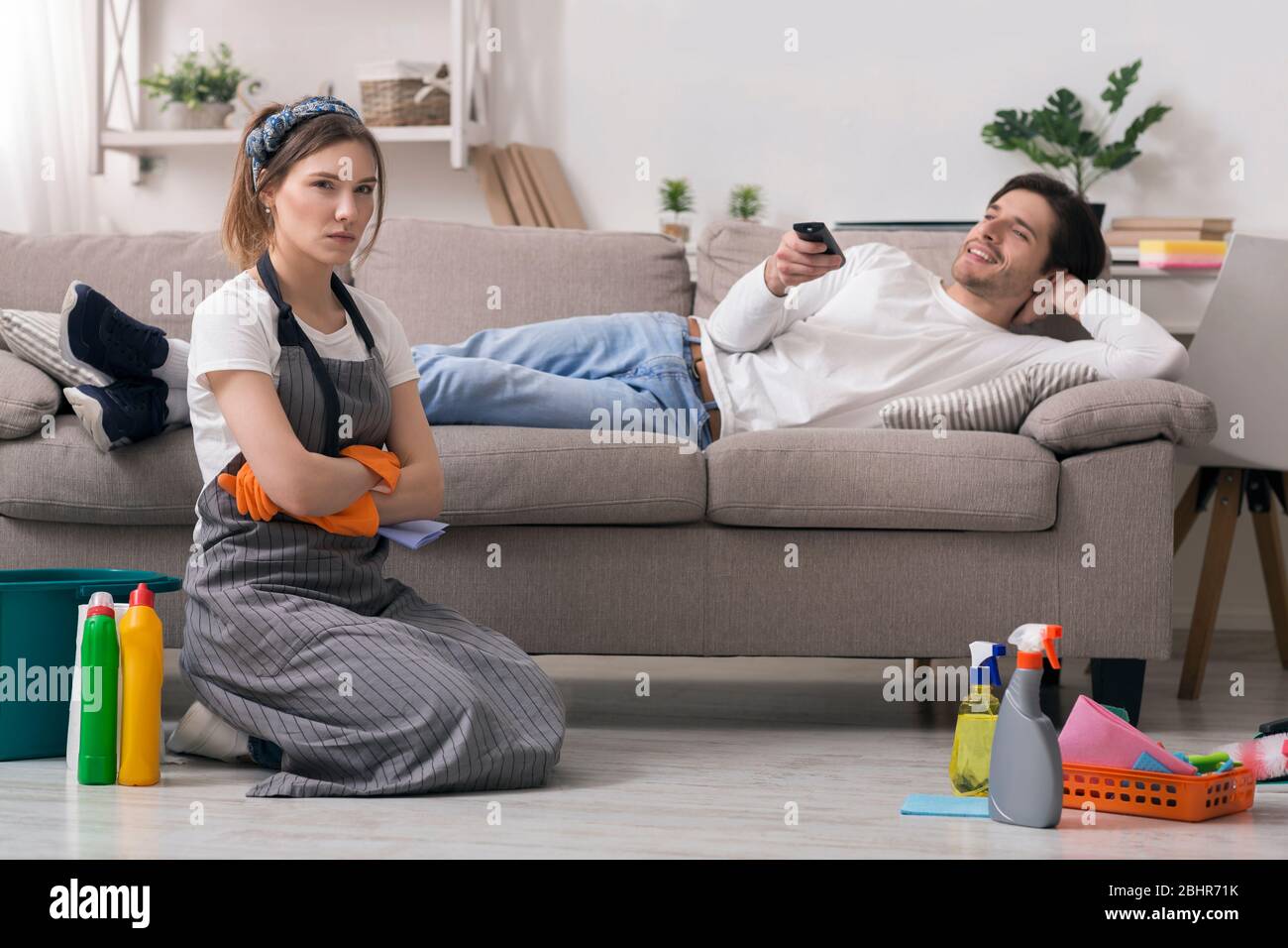 Tareas domésticas. Mujer ofendida cansada después de la limpieza sentada junto a un marido perezoso Foto de stock