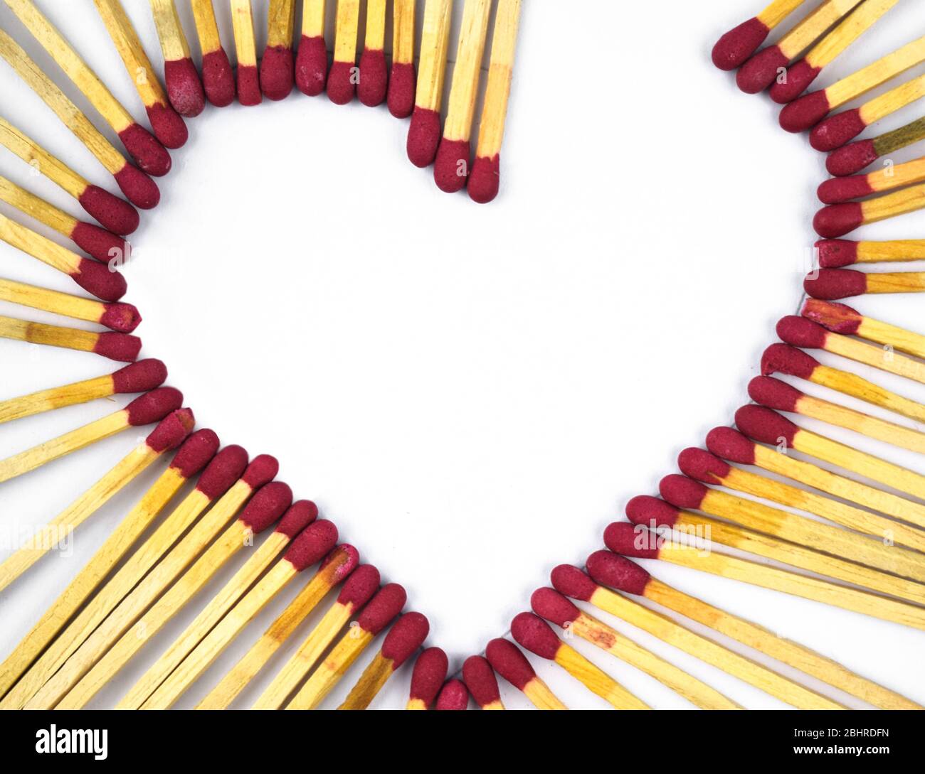 Corazón roto hecho con palos de color rojo quemados frente a un fondo blanco aislado Foto de stock
