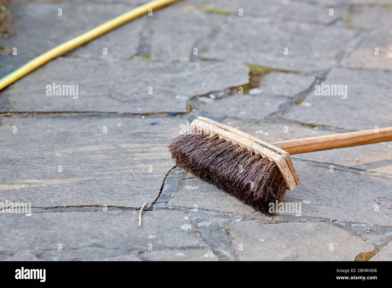 Escoba vieja usada y manguera de riego amarilla sobre piedras de pavimento  en un jardín. Visto en Alemania en abril Fotografía de stock - Alamy