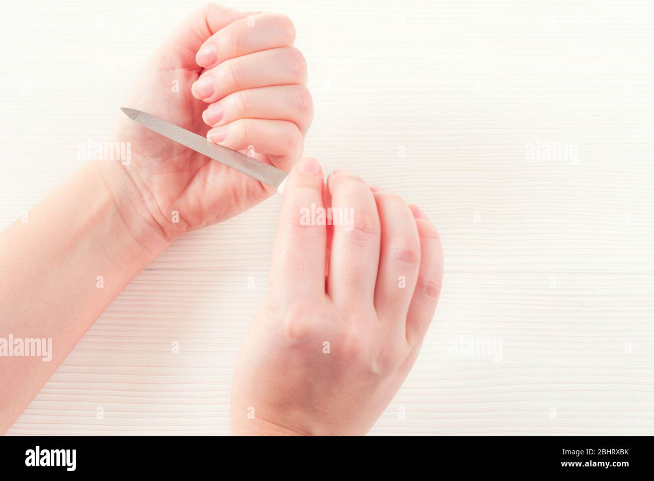 Mano de la mujer blanca con uñas naturales sanas procedimiento para el cuidado de la uña. Manos blancas, hembras, pulimentas uñas con lima de uñas, aisladas sobre blanco Foto de stock