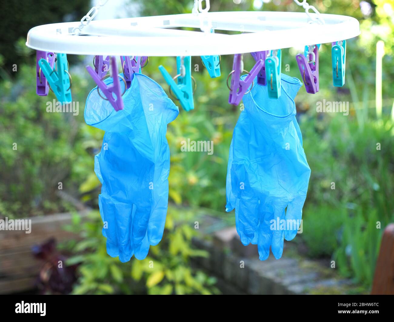 Vista de un par de guantes quirúrgicos azules reutilizables que cuelgan hasta secarse después de ser lavados durante la pandemia del coronavirus de 2020 Foto de stock