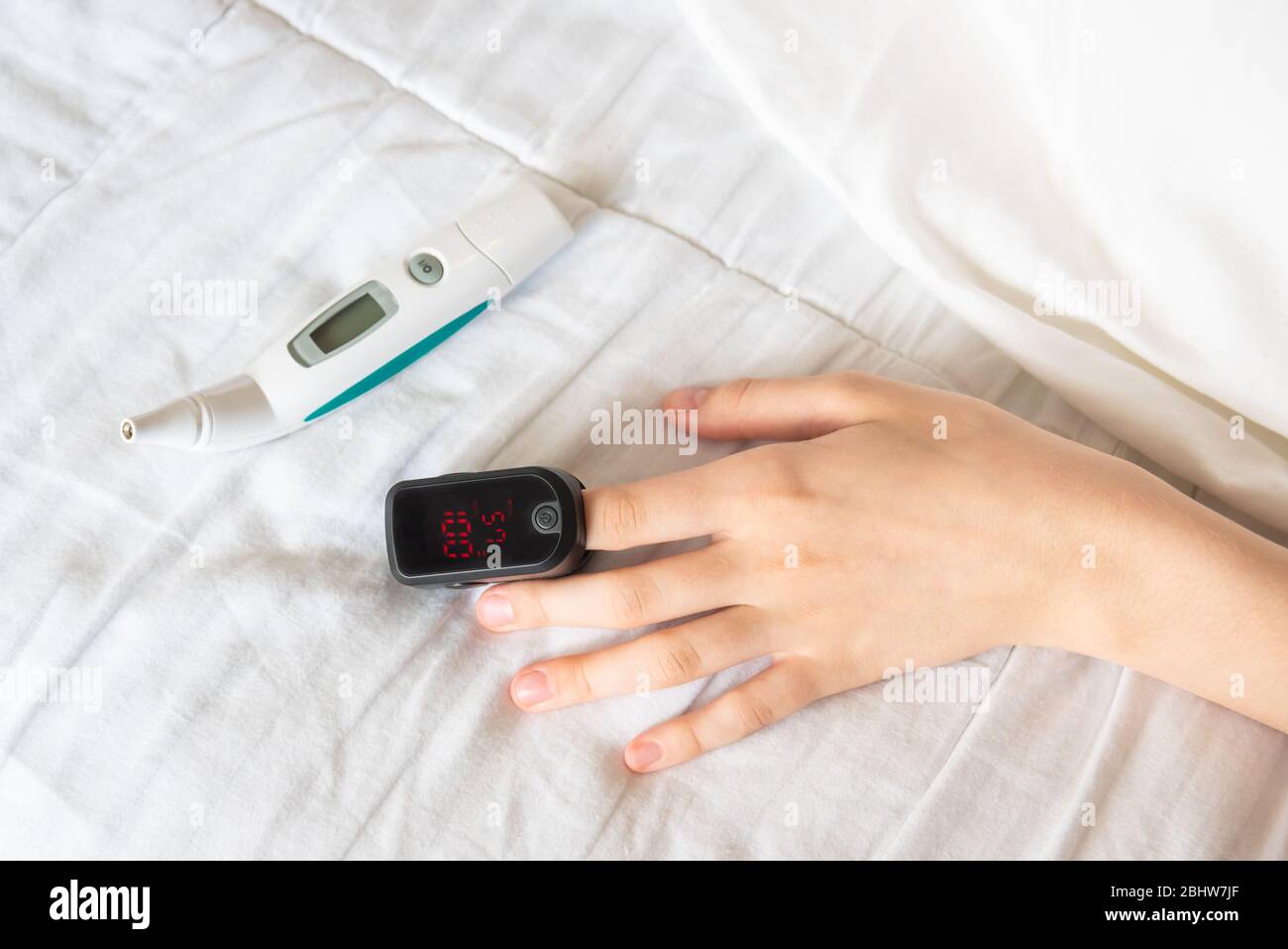 Primer plano de la mano de la mujer usando pulsioxímetro en el dedo con termómetro digital en la cama Foto de stock