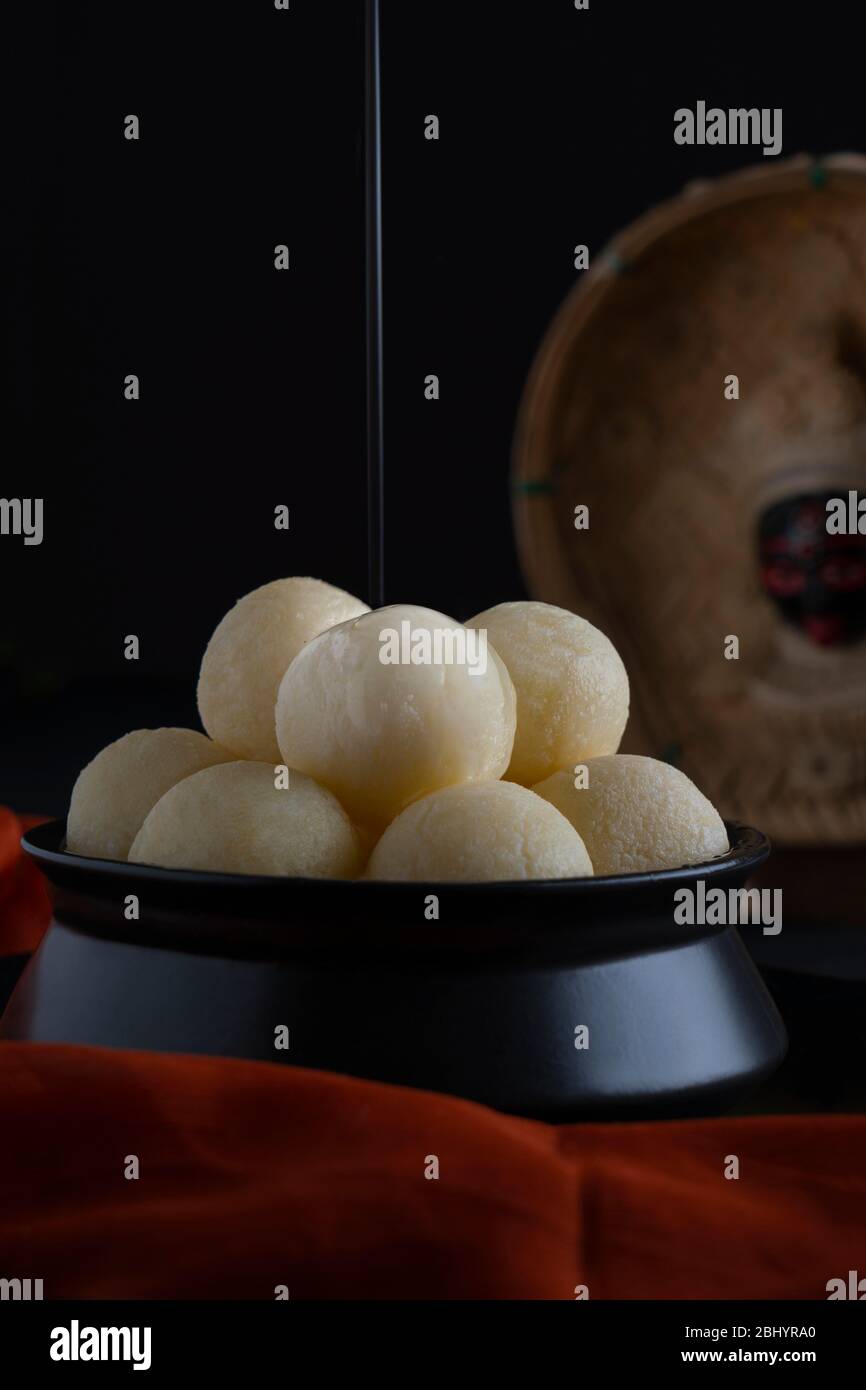 Cerca de boca regando rasgullas blancas guardadas en un tazón negro con jarabe de azúcar goteando en la parte superior. Foto de stock