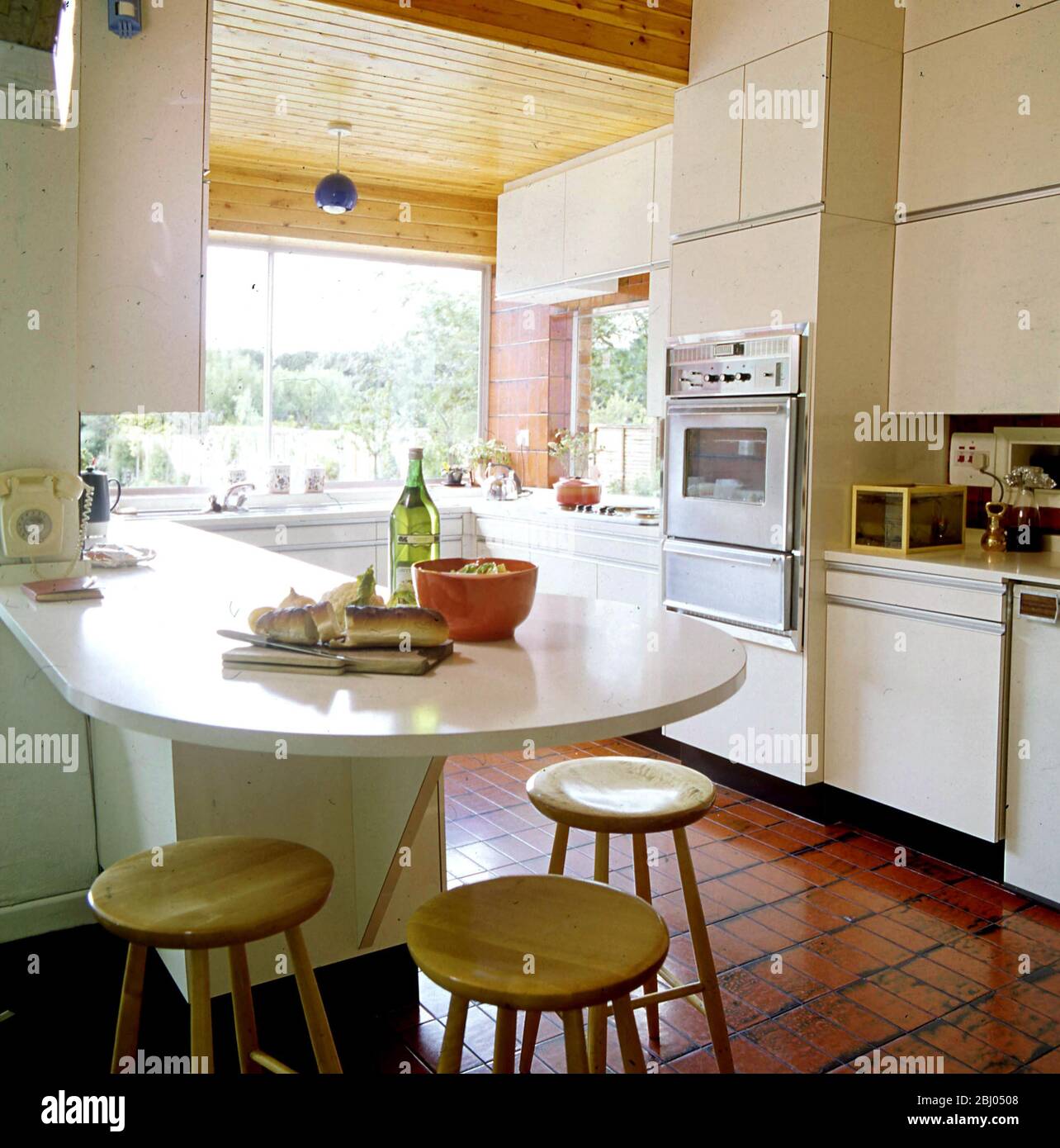 Cocina 1960(?) con barra de desayuno, piso de baldosas, techo de madera y horno montado en la pared - - Foto de stock