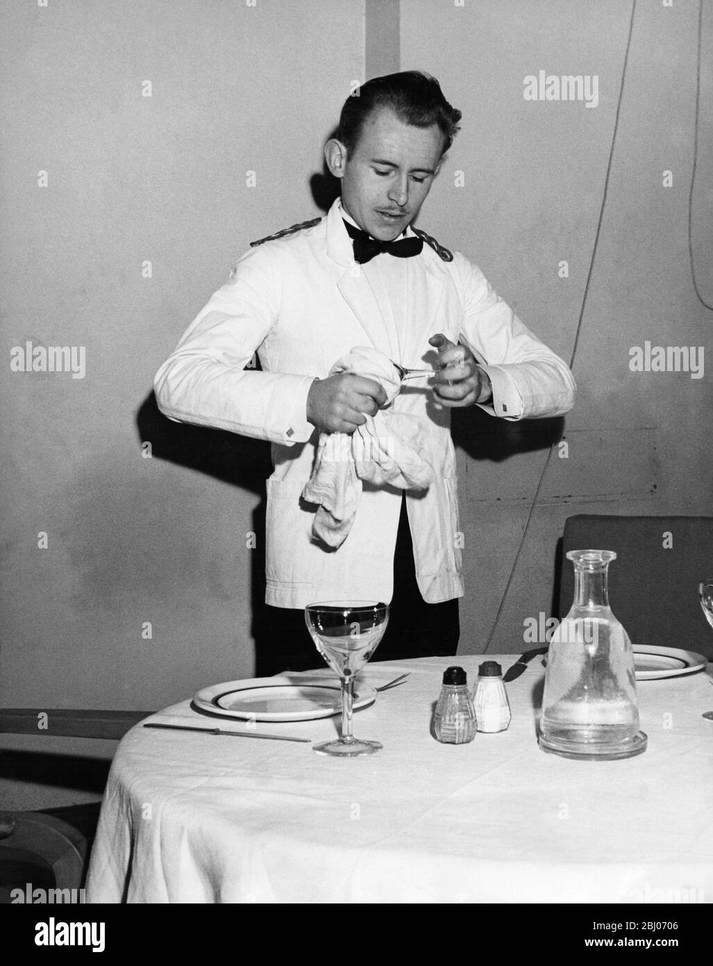 Un camarero pule un vaso mientras prepara la mesa para los comensales del restaurante por las noches Foto de stock