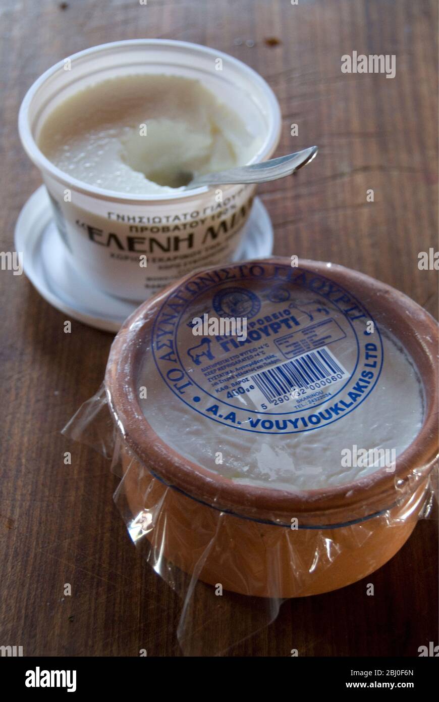 Cartón de plástico de griego set de leche de vaca yogur y plato de cerámica de leche de oveja yogur en la barra de la cocina en la casa chipriota - Foto de stock