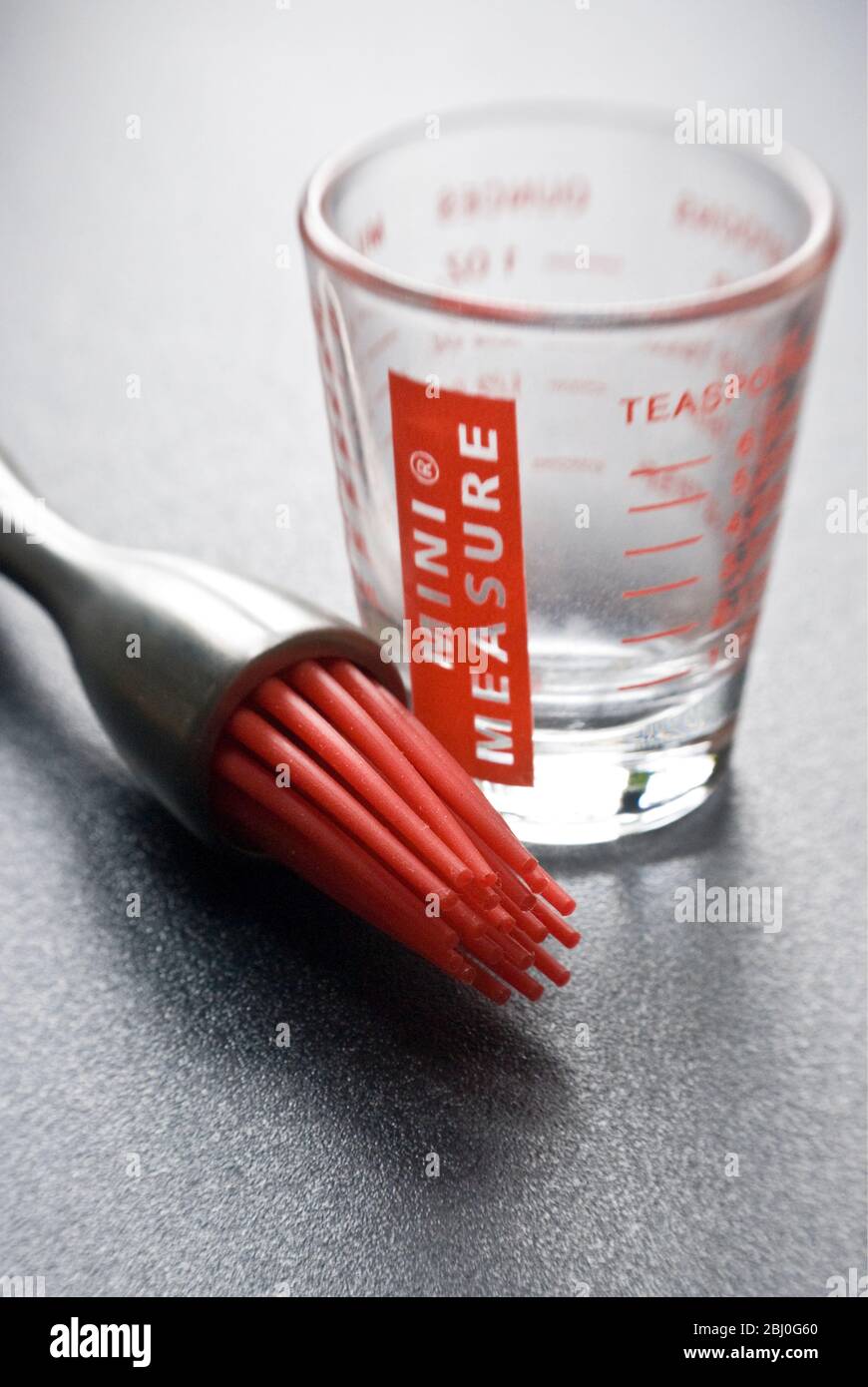 Cepillo de repostería moderno con "cerdas" de silicona roja con un poco de cristal de medición sobre una superficie texturizada oscura - Foto de stock
