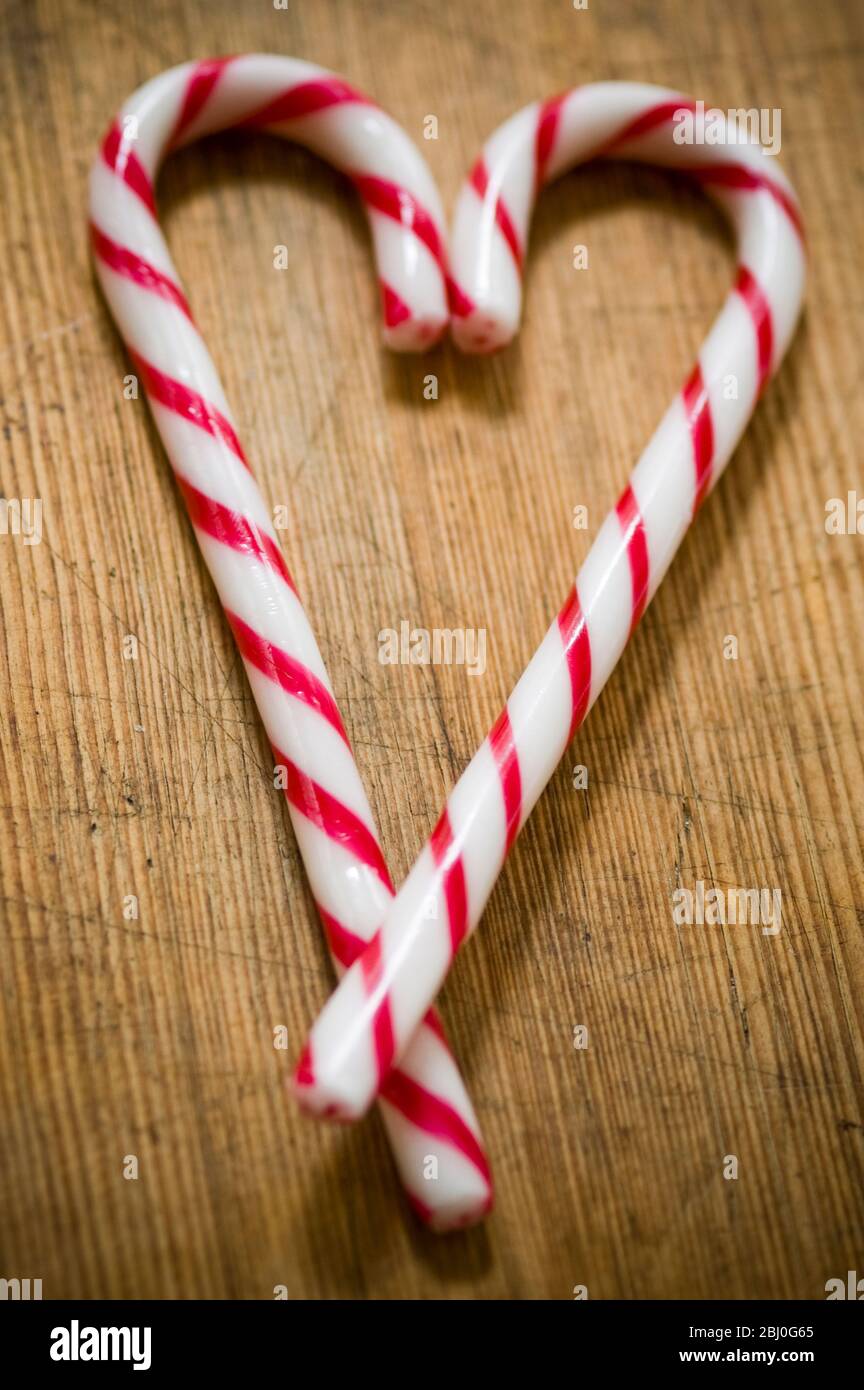 Dos bastones de caramelo a rayas rojas y blancas en la superficie de madera cruzados para formar el corazón. - Foto de stock