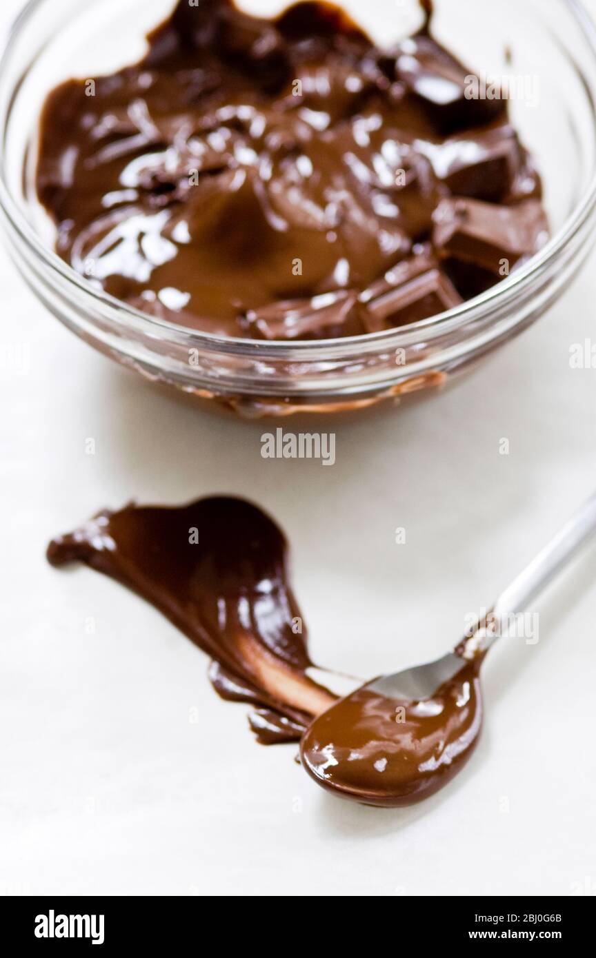 Cuenco de cristal de chocolate fundido con cuchara impregnado de chocolate sobre superficie blanca - Foto de stock