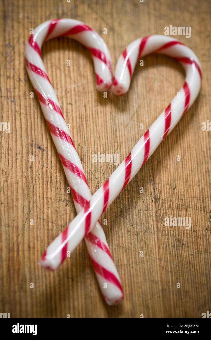 Dos bastones de caramelo a rayas rojas y blancas en la superficie de madera cruzados para formar el corazón. - Foto de stock