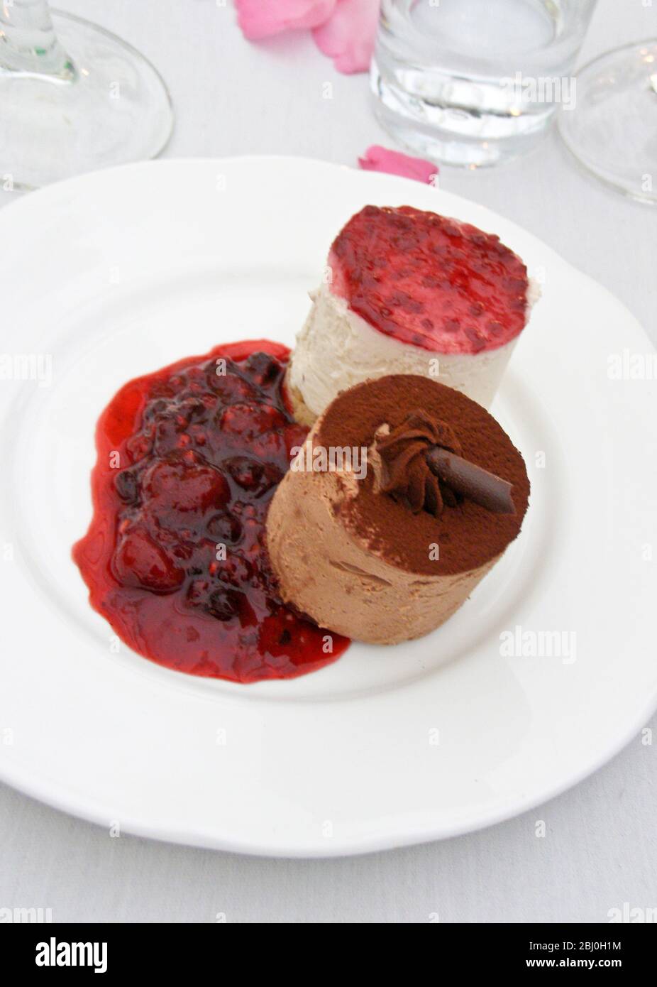 Mousses de chocolate y vainilla con coulis de frutos de verano - postre en recepción de boda - Foto de stock