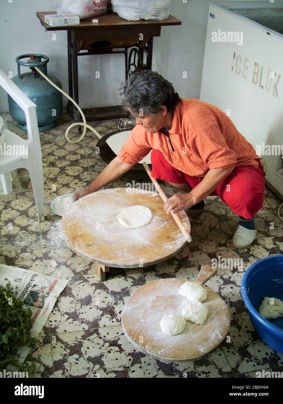 Panadero turco que rodaba grandes y delgados círculos de pan en una tabla redonda de madera en el suelo de la panadería Quayside. Detrás está el calentador de gas que ella Foto de stock