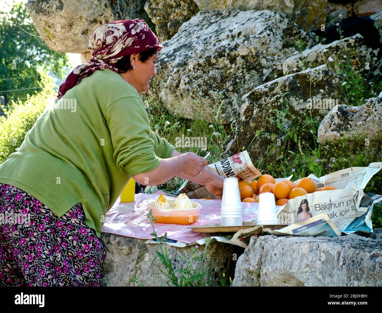 Mujer exprimiendo naranjas para vender vasos de jugo fresco a los turistas en el antiguo anfiteatro griego, el sur de Turquía - Foto de stock