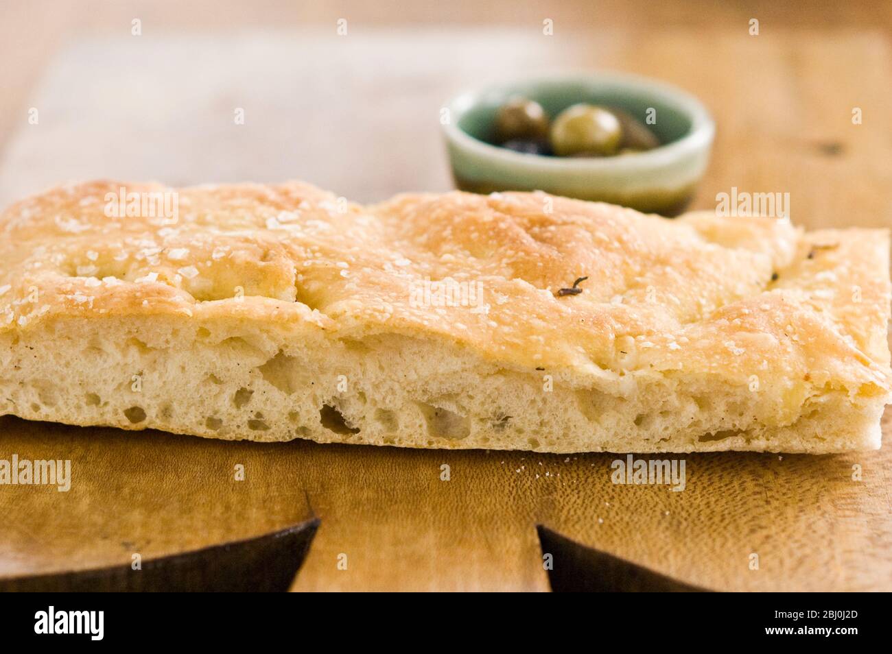 Aceite de oliva y romero foccaccia pan sobre tabla de madera con pequeños tazones de aceite de oliva herbed y aceitunas enteras. - Foto de stock