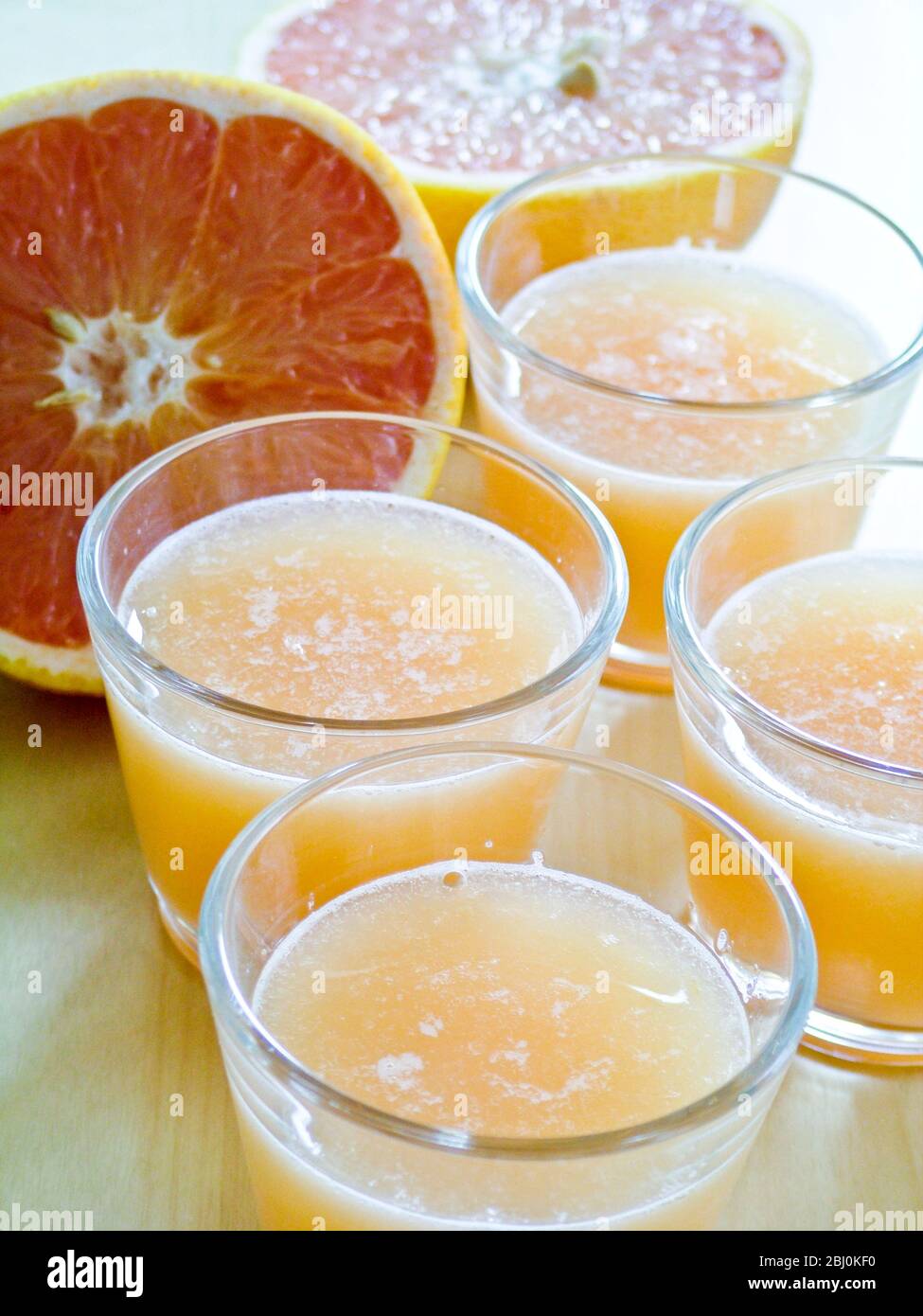 Vasos pequeños de jugo de pomelo rosado con pomelo entero y mitad reducido - Foto de stock