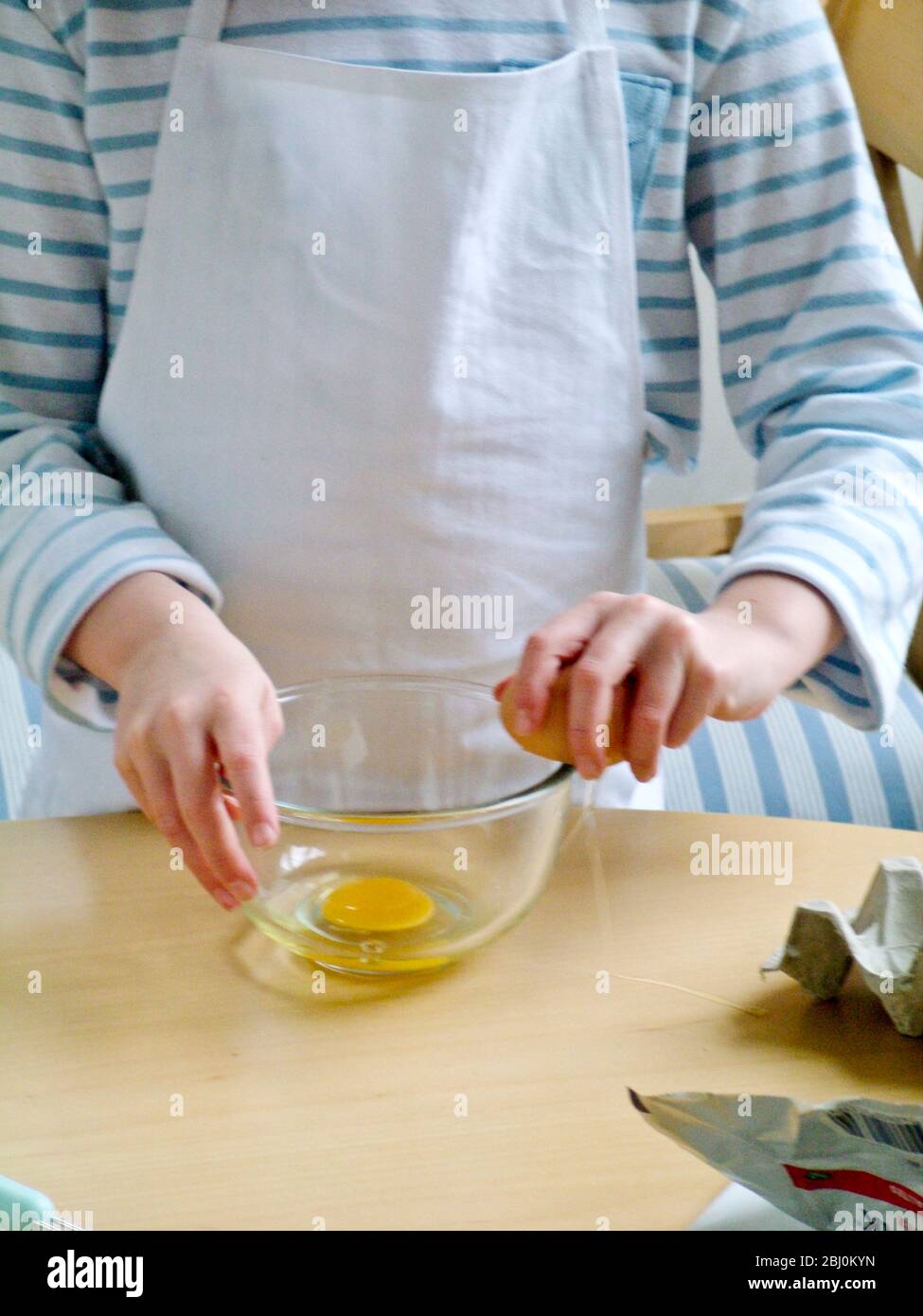 Niño rompiendo huevos en un tazón de vidrio, aprendiendo a hacer huevos revueltos. - Foto de stock