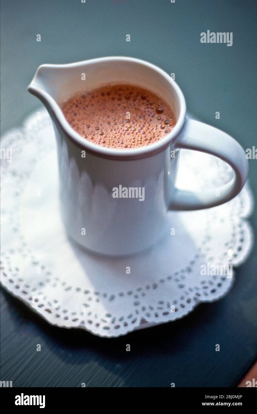 Jarra de chocolate caliente para beber sobre papel blanco encaje doiley - Foto de stock