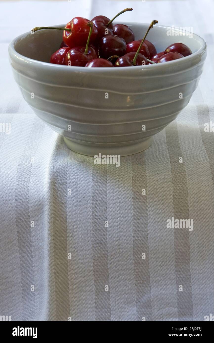 Cuenco de cerezas en cuenco de cerámica gris sobre tela de lino a rayas - Foto de stock
