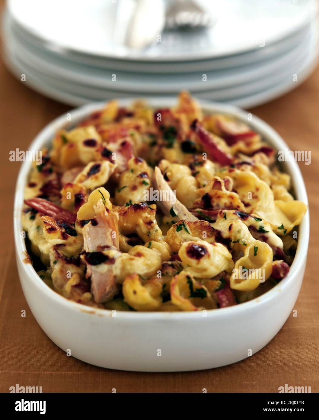 Pasta y pavo hornean para usar las sobras navideñas en un plato del horno con un montón de platos blancos - Foto de stock