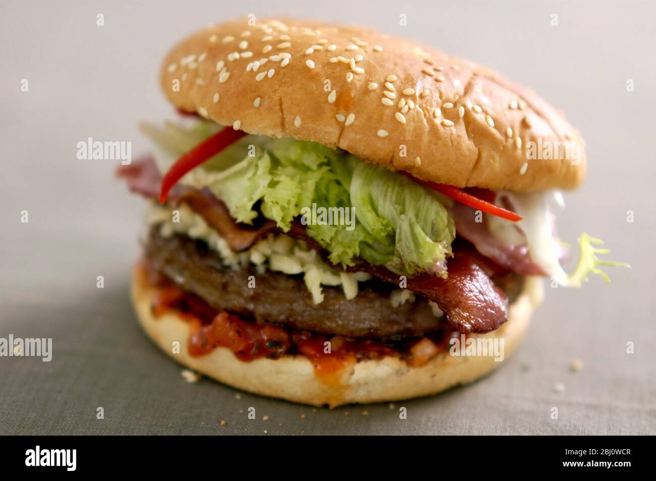 Hamburguesas a la parrilla en bollo con ensalada de frisee, salsa de tomate y queso, tocino y tiras de pimienta - - Foto de stock